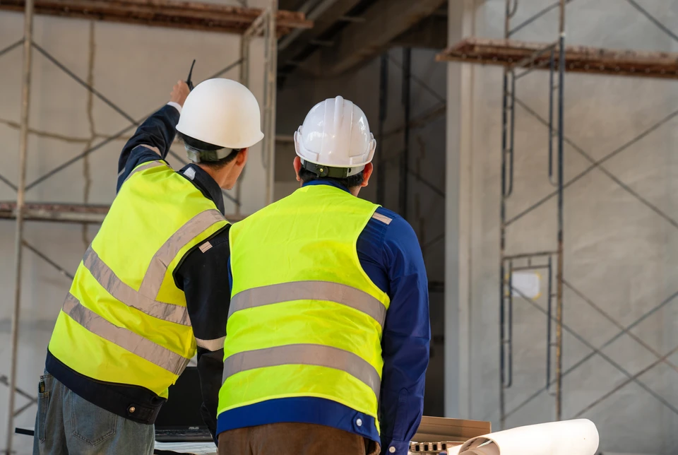 Deux ouvriers en casque de chantier installent une poutre en bois dans un bâtiment en construction